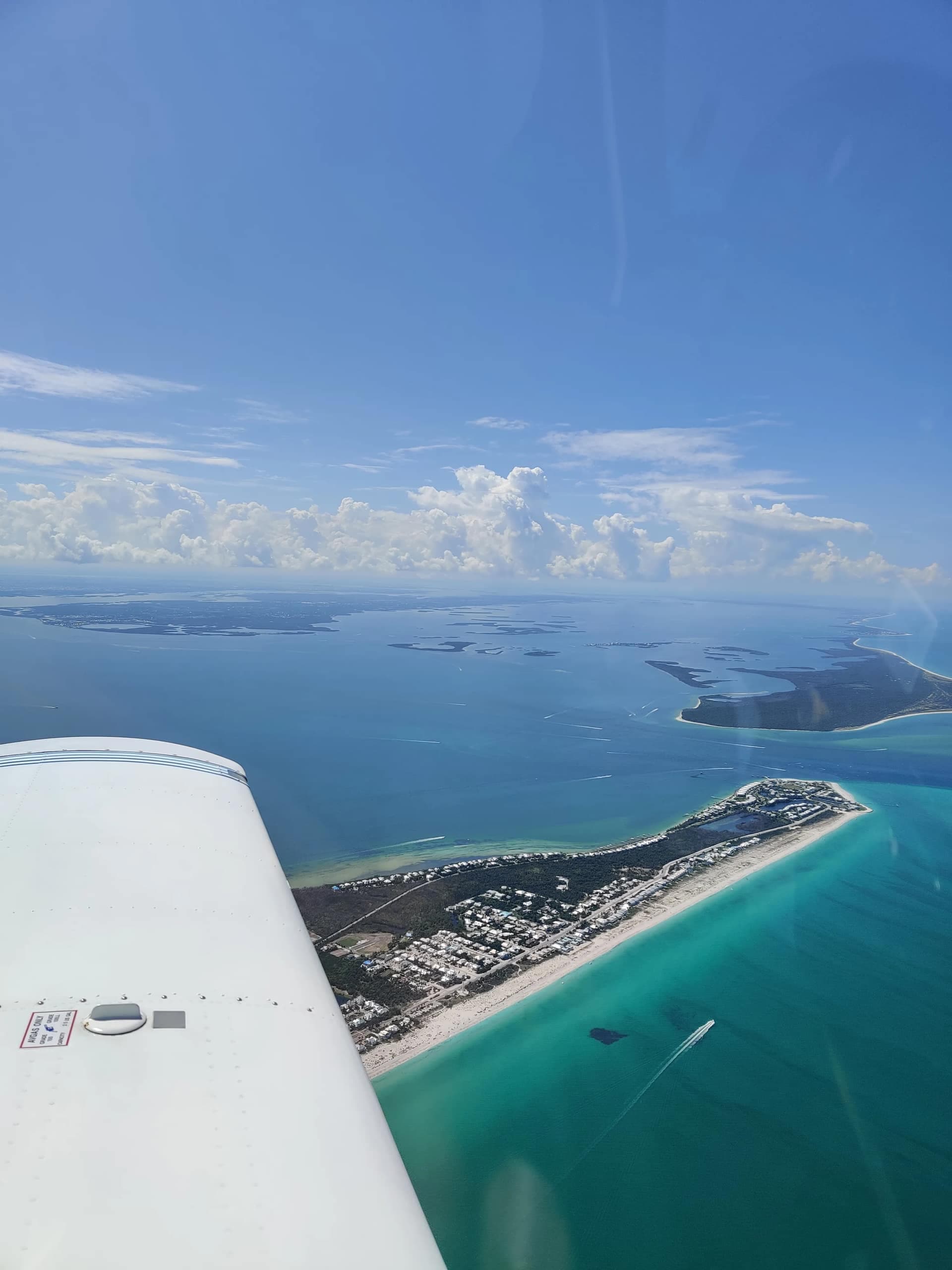 View over the wing of the Cherokee: turquoise Gulf water, a white-sand barrier island, and the Southwest Florida coastline