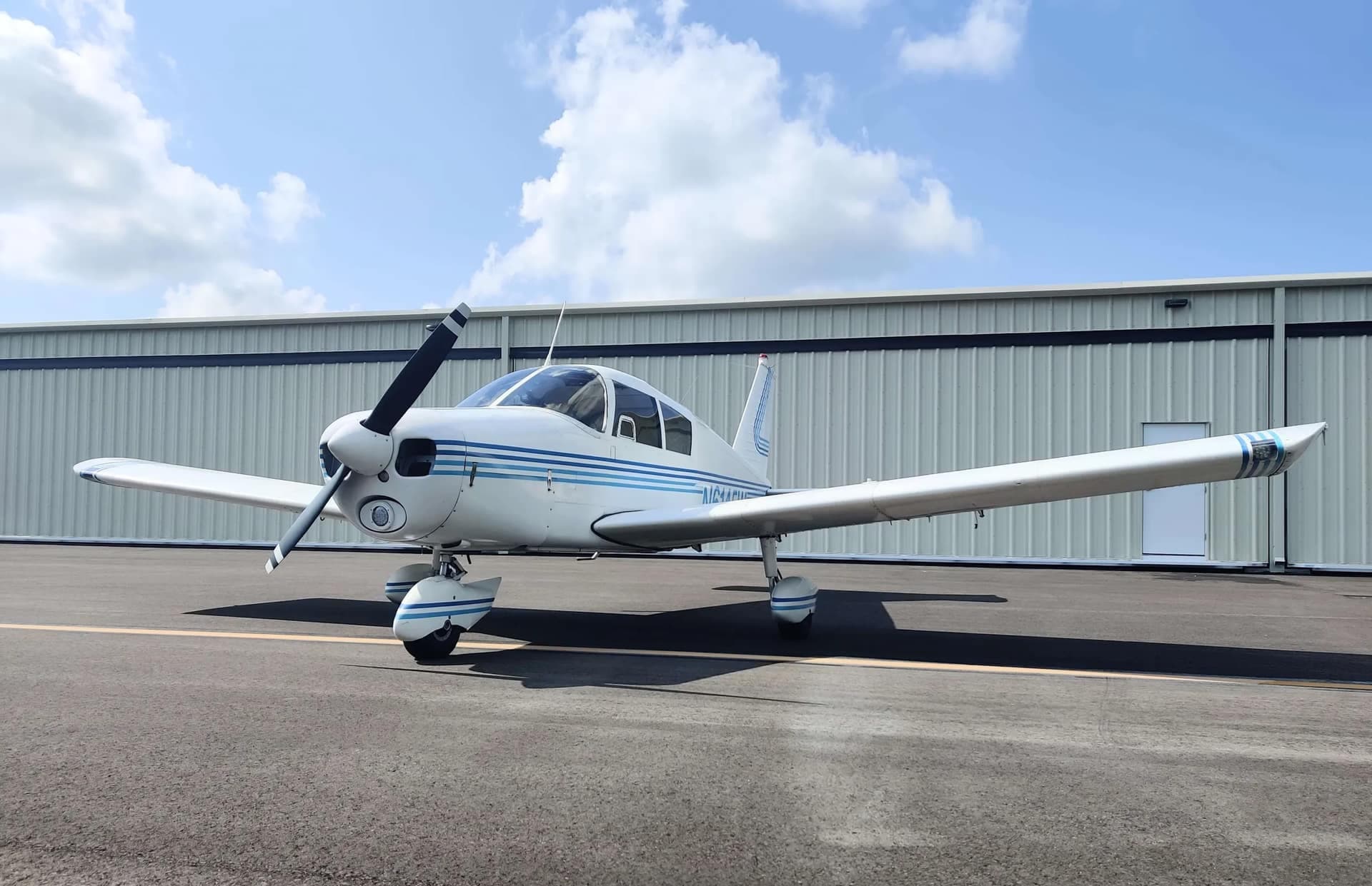 The school’s Piper Cherokee 140 parked on the ramp at Page Field, hangar line behind it